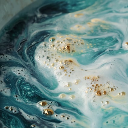 Nahaufnahme einer ozeanblau-weißen, mit Seifenblasen gefüllten Badewanne, verziert mit goldenem Glitzer für zusätzlichen Glanz. Die Szene wurde von oben aufgenommen und zeigt die komplizierten Details sowohl in den wirbelnden Mustern