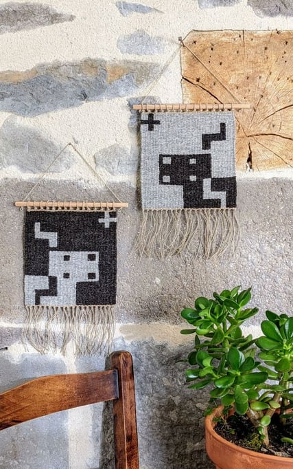 Sur une terrasse le kilim-tenture murale en tissage pixelisé représentant un écureuil sur le fond de la laine gris foncé est accroché sur un volet à côté de la fenêtre. Dessin du tissage mural géométrisé.