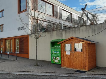 Holzhütte vor Betonwand daneben Kleidercontainer