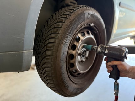 alt="Nahaufnahme eines Autoreifens beim Reifenwechsel mit sichtbaren Schlagschrauber und einer Hand"