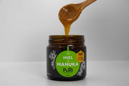 Miel de Manuka NPA 10+ Puri New Zealand avec une cuillère en bois et du Miel qui coule dans le pot sous fond blanc