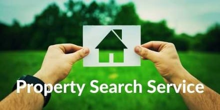 Someone holding a cut out of a house while looking at a green garden