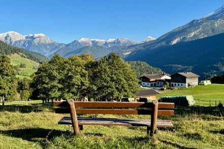 Blick auf die Berge mit einer leeren Sitzbank im Vordergrund bei klarem Himmel.