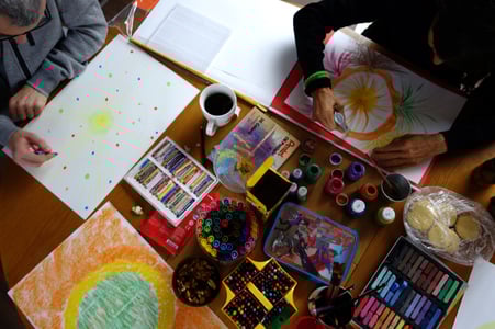 Mesa con materiales de arte y dos personas dibujando