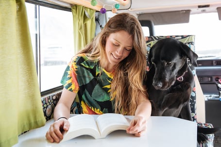 Im Wohnmobil: Eine Frau mit langen Haaren und Buch und ein Labrador sitzen zusammen.