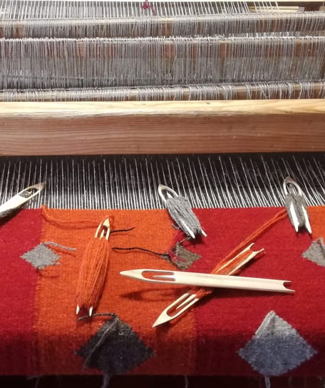 Tapis kilim est sur le métier en train d'être tissé à la main, il a fond rouge et orange et le motif des diamants gris. Les petites navettes en bois avec les laines en couleurs sont posées sur le tissage. Les fils de la chaîne en lin sont visibles.
