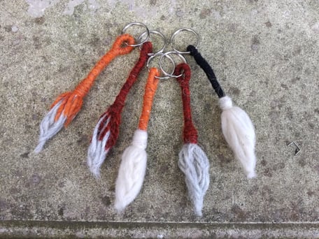 Cinq porte-clés en forme de queue de vache Salers faits avec la laine orange, marronne, noire et blanche sont exposés sur un fond en béton. 