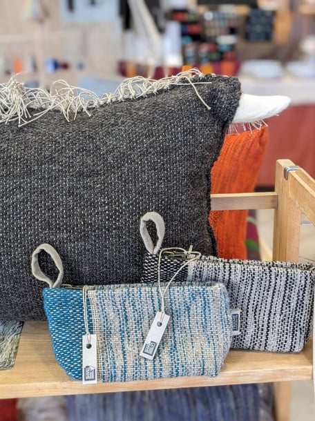 Deux trousses tissées en laine sont rangées une après l'autre - la première est bleue, la deuxième noire, devant un grand coussin noir.