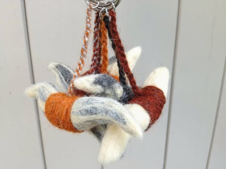 Cinq porte-clés en forme de cornes de vache Salers faits avec la laine feutrée orange, marronne, noire et blanche sont exposés en bouquet sur un fond en bois gris. 