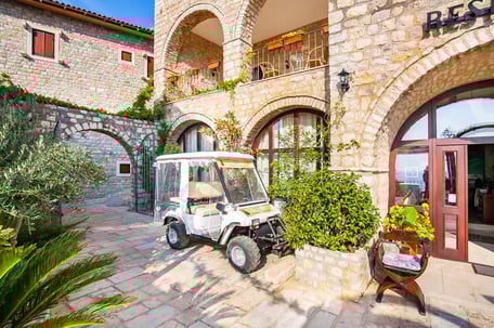 White golf cart parked in the courtyard of a traditional stone building of Palata Venezia Ulcinj Hotel with arched entrances and Mediterranean landscaping
