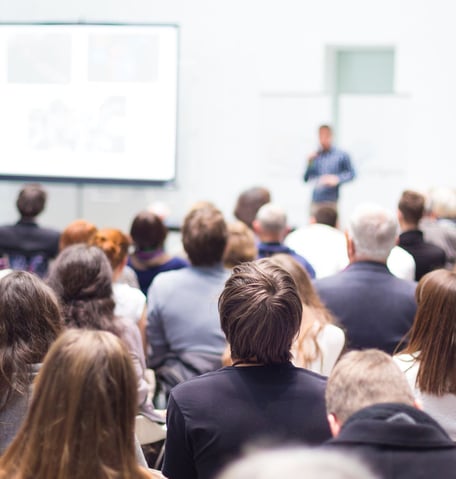 Personen sitzen in einem Raum und hören einem Vortrag zu.