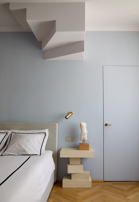 La master bedroom è caratterizzata dal profilo aggettante della scala che conduce al livello superiore. Un tempo era nascosta da una trave ma i progettisti hanno deciso di metterla in mostra, come elemento onirico, un accento quasi installativo.