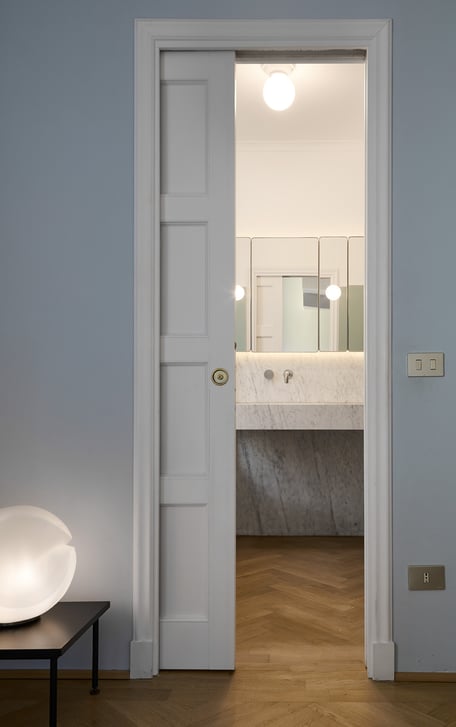 Vista del bagno en suite, una rigorosa composizione in marmo di Carrara con specchieta/contenitore su disegno e pannelli con applique incastonate.