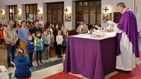 Beim Erneuern des Taufversprechens halten die Kinder ihre Taufkerzen in der Hand und die Taufpaten stehen hinter ihnen.