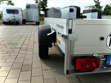 alt="Silberner, offener Einachsiger Anhänger, auf einem ebenen Untergrund"