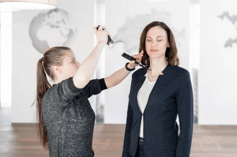 Visagistin fixiert Haare von Geschäftsfrau mit Haarspray für Fotos