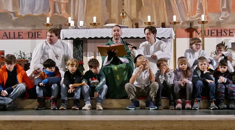 Kaplan Pawel liest das Evangelium von den Menschenfischern sitzend bei den Kindern auf der Stufe vor dem Altar.