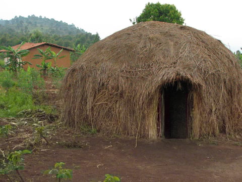 Tipica capanna Batwa con sullo sfondo una nuova casa.