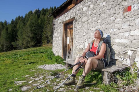Wanderin sitzt entspannt, mit geschlossenen Augen, auf einer Bank vor einer Schutzhütte