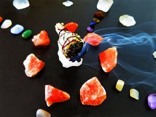 Auch schwarzem Untergrund sind Steine im Stil des schamanischen Medizinrades angeordnet, auf dem grossen Stein in der Mitte liegt ein weisser Salbei Rauchbündel, es kommt Rauch vom Salbeibündel