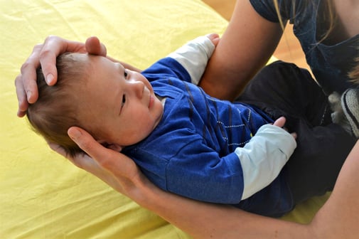 CranioSacral Therapeutin hält ein Baby in den Armen und legt die Hände sanft auf den Kopf des Neugeborenen, um Blockaden zu lösen und dem Kind so zu einem besseren Schlaf zu verhelfen.