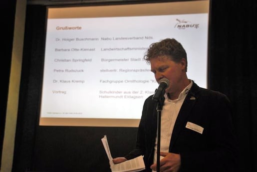 Hr. Buschmann auf einer kleinen Bühne mit einer Präsentation im Hintergrund