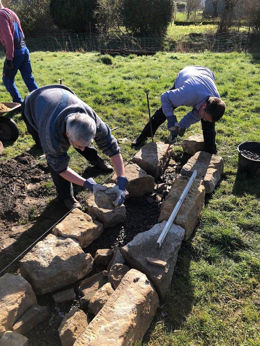 Nahaufnahme der ersten Steinreihe, zwei Männer platzieren die Steine mit den Händen