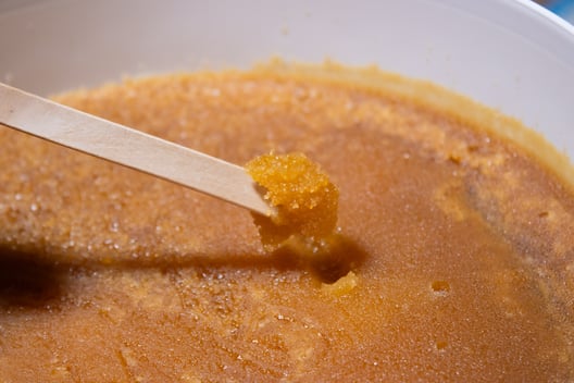 Photo d'un Miel de Kanuka de Nouvelle-Zélande cristallisé en seau de 10 kg pour les professionnels et grossistes, une cuillère en bois dans la quelle se trouve le Miel 