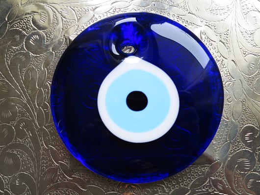 Ein grosses blaues Nazar Glas Auge liegt auf einem metall Teller der schön verziert ist. Nahaufname und glänzend