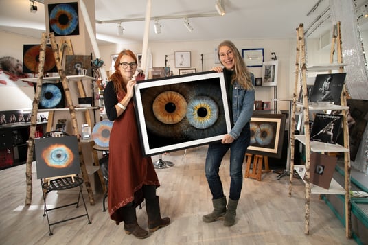 Das Team H2Fotografie hält gemeinsam ein großes Bild mit dem Kunstwerk "Irisfotografie" fest. Im Hintergrund ist der freundlich-helle Verkaufsraum von H2Fotografie zu sehen.