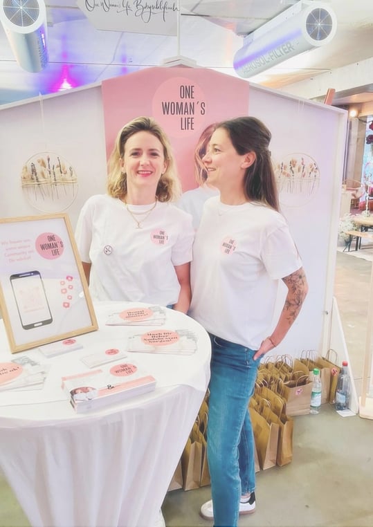 Messestand von One Woman’s Life mit den zwei Gründerinnen und ihrem Markenauftritt – Beispiel für Corporate Design, Standgestaltung und Markenpräsentation.