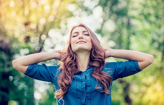 森林の中で新鮮な空気に包まれ気持ちよさそうな女性