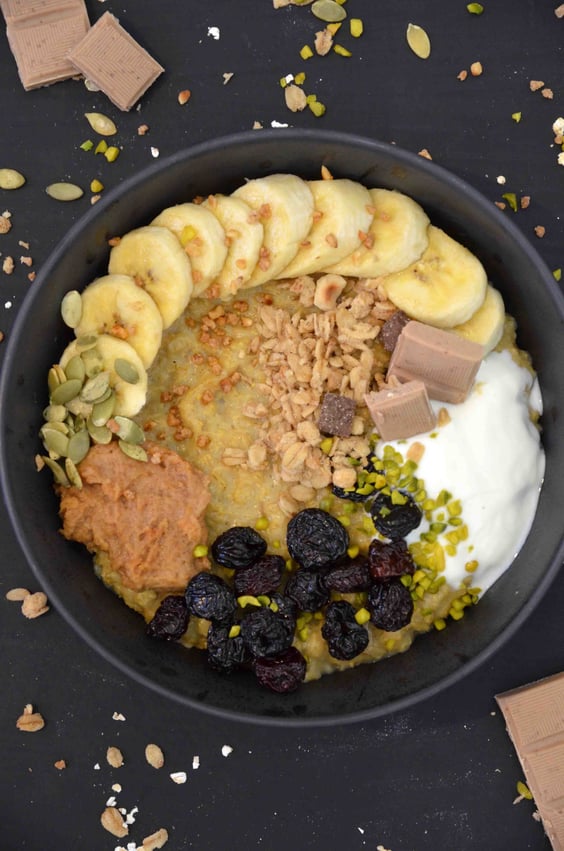 Schottisches Porridge - vegan -, getoppt mit Banane, Schokolade, Erdnussbutter, veganem Joghurt, Kürbiskernen, Granola, Pistazien