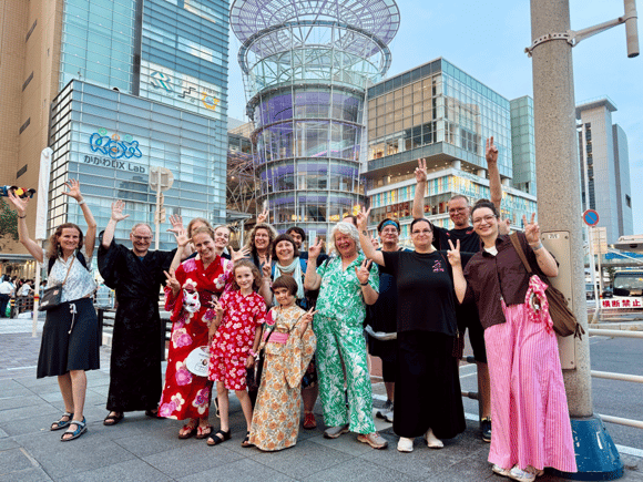 Bunt gekleidete, fröhliche Menschen posieren gemeinsam vor einem Gläsernen Gebäudekomplex