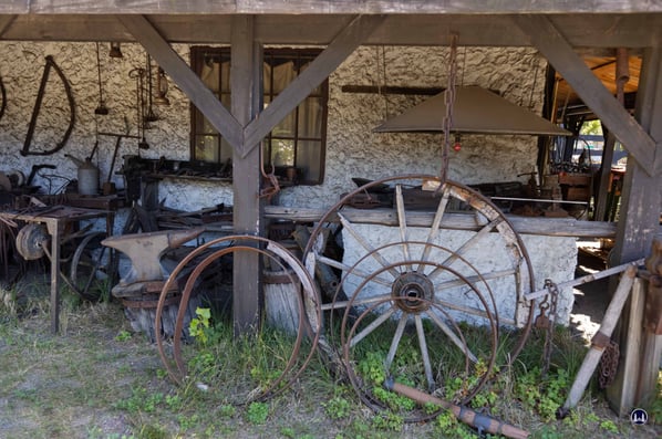 Amboss (links) und eine Schmiedeesse (im Hintergrund rechts) sind typische Ausrüstungsgegenstände eines Blacksmith. Ein paar alte Radreifen für all die Kutschen jener Epoche galt es stehts anzufertigen oder zu reparieren.