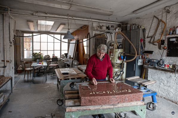 Herr Damerau beim Setzen von Buchstaben auf einem Grabstein.