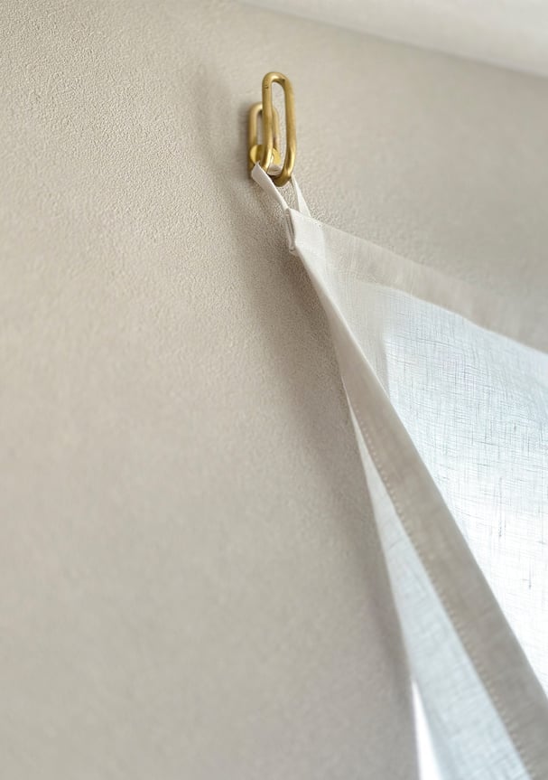 ふさかけに直接引っ掛けられるよう縫製されたリネンカーテン。金具に軽やかに掛かる様子