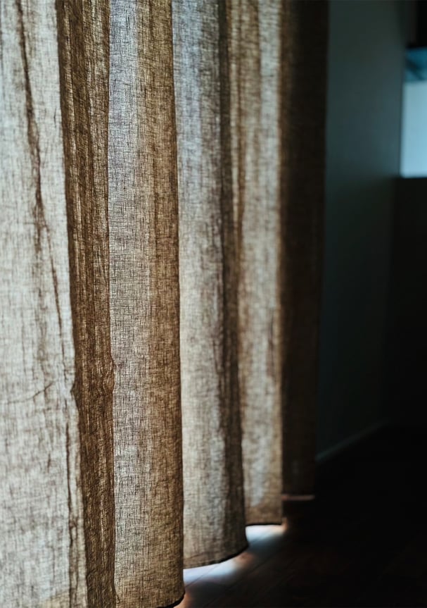 アッシュカーキのリネンカーテンが光を受けて陰影を作る。素材の織りが際立つ繊細な質感。