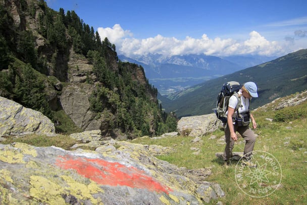 Wanderin passiert rote Wegmarkierung im Hintergrund traumhaftes Bergpanorama