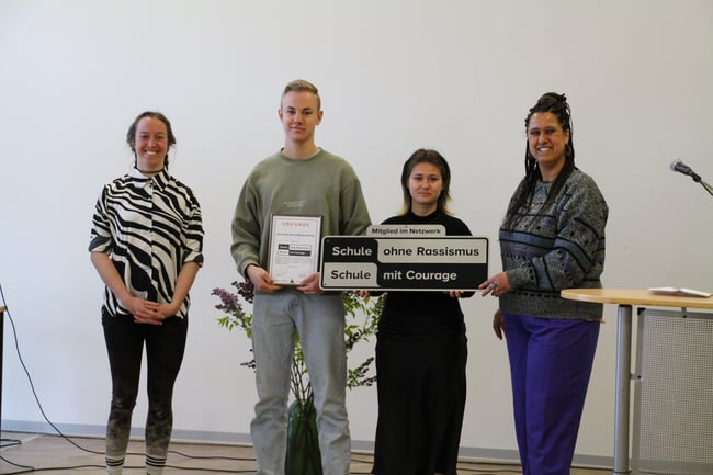 Die Landeskoordinatorinnen Frau Dailey und Frau Lohmann überreichen die Plakette an die Schülersprecher Valeria und Täve.