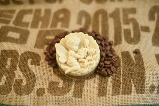 Das Bild zeigt eine Kaffeeseife Schutzengel auf Kaffeebohnen von Schneider Kaffee und einen Jutesack