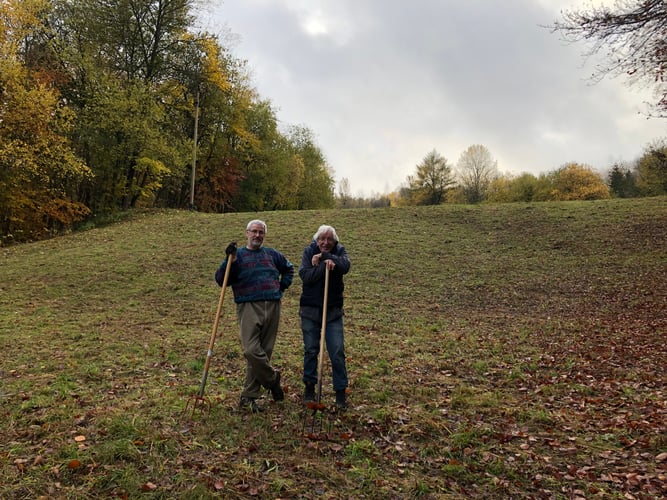 Zwei Helfer posieren gut gelaunt auf der Skiwiese mit Heugabeln