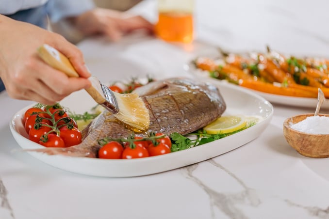 Image d'une personne préparant un repas à base de poisson, légumes, à l'aide d'un pinceau il badigeonne le dessus du poisson avec un Miel de Manuka de Nouvelle-Zélande pour le sublimer