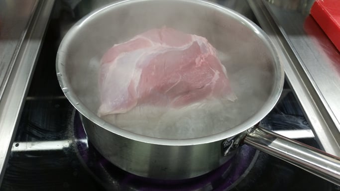 a) Einen Topf mit zirka 2 cm Wasser zum Kochen bringen und die Schweineschulter mit der Schwarte voraus in das Wasser geben.