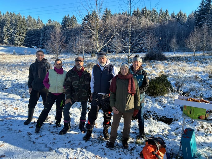 6 Menschen stehen im Vordergrund während dahinter eine vereiste Landschaft mit Häufen an Verbuschungsmaterial zu sehen ist.