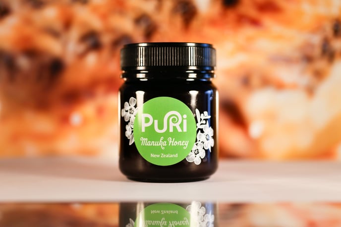 Pot de Miel de Manuka / Manuka Honey Puri New Zealand en Nouvelle-Zélande sous fond avec un cadre de Miel et des abeilles, le pot se reflète dans un mirroir dessous