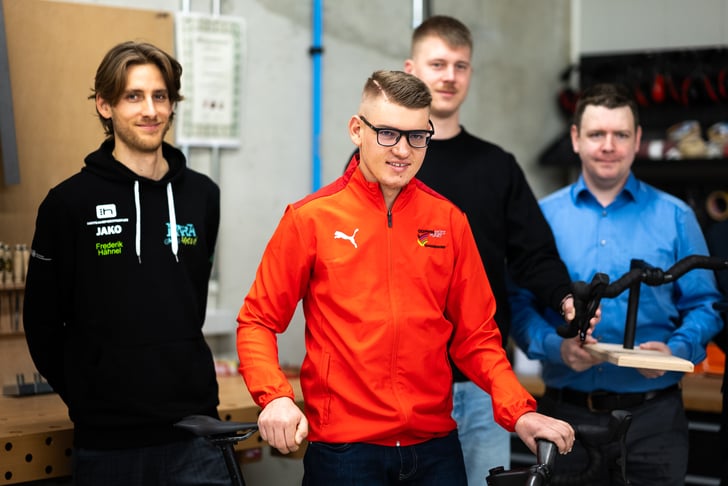 (v.l.n.r.) Frederik Hähnel (Lehrertrainer Para-Radsport), Eyke Heinze (Werkstattleiter des COLab), Oliver Dorn (wissenschaftlicher Mitarbeiter am Fachgebiet Polymerbasierter Leichtbau) mit Paracycler Maximilian Jäger (vorn Mitte) © COLab/ Kenneth Marter