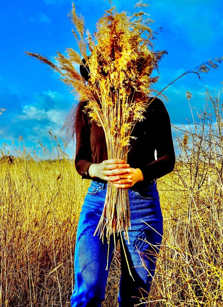 Eine Frau steht bei strahlendem Himmerl in einem Getreidefeld und hält sich einen Bund davon vor das Gesicht. 