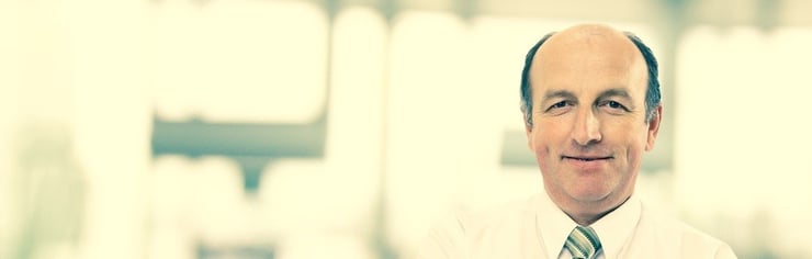 45 jähriger, freundlich aussehender Mann mit Glatze. Trägt weisses Hemd mit gestreifter Krawatte.