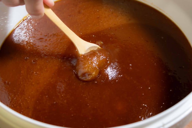 Texture naturelle d'un Miel de Manuka NPA 24+ / MGO 1122+ de Nouvelle-Zélande dans son seau de 10kg avec une cuillère en bois plantée dedans